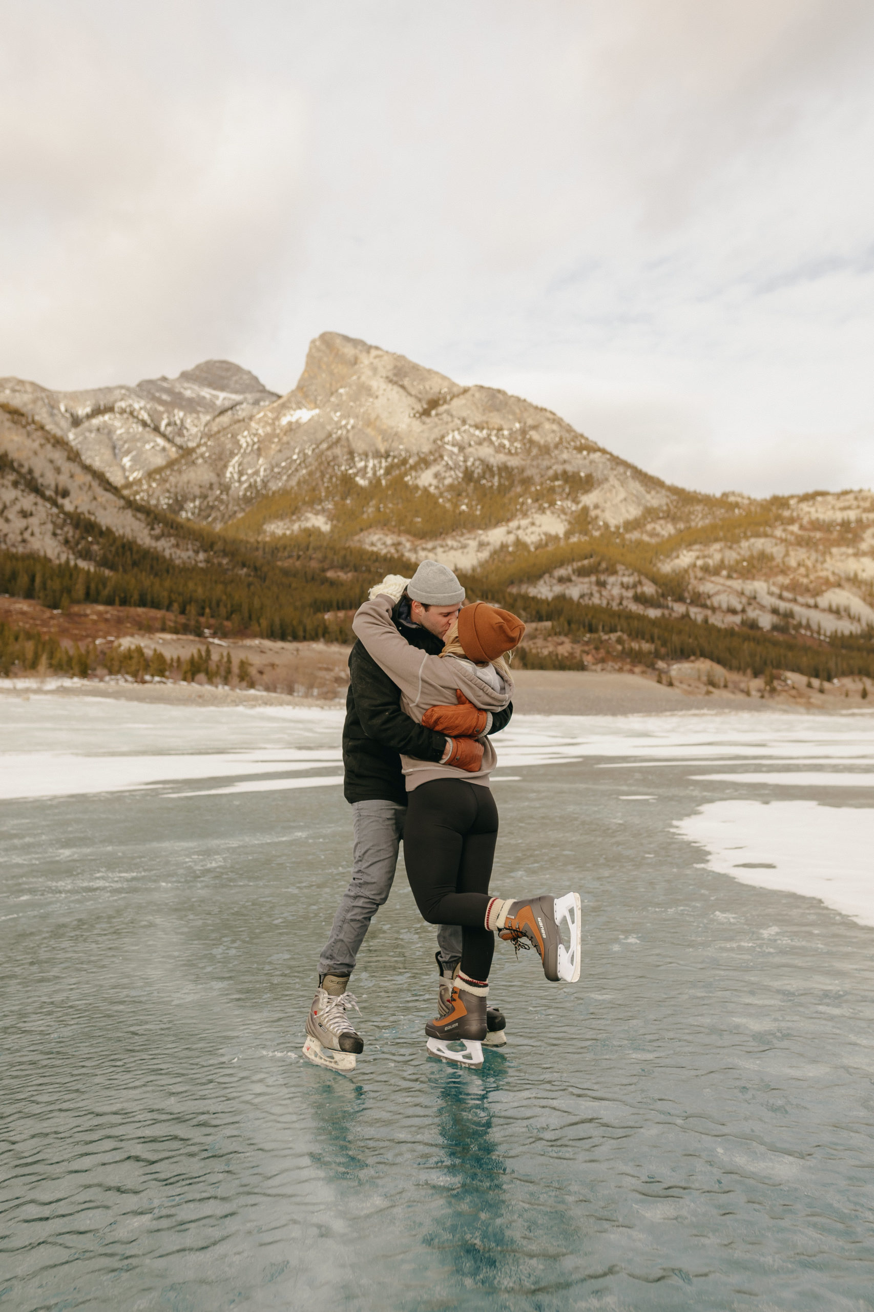 couple ice skating & kissing on mountain lake