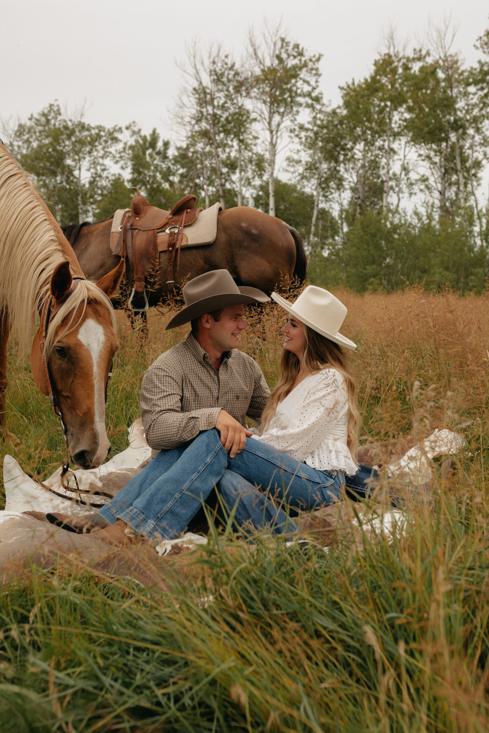 cowboy and cowgirl sitting in the tall grass surrounded by horses