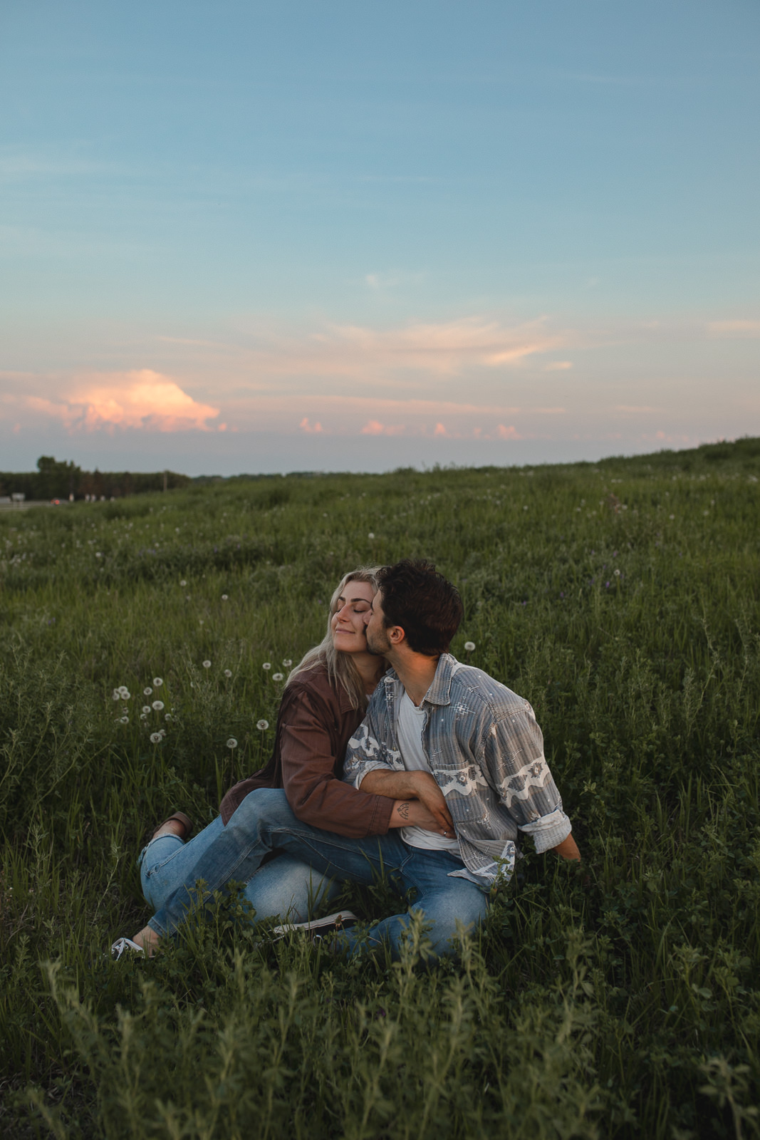 Man kissing woman on cheek, sitting in rolling fields of grass