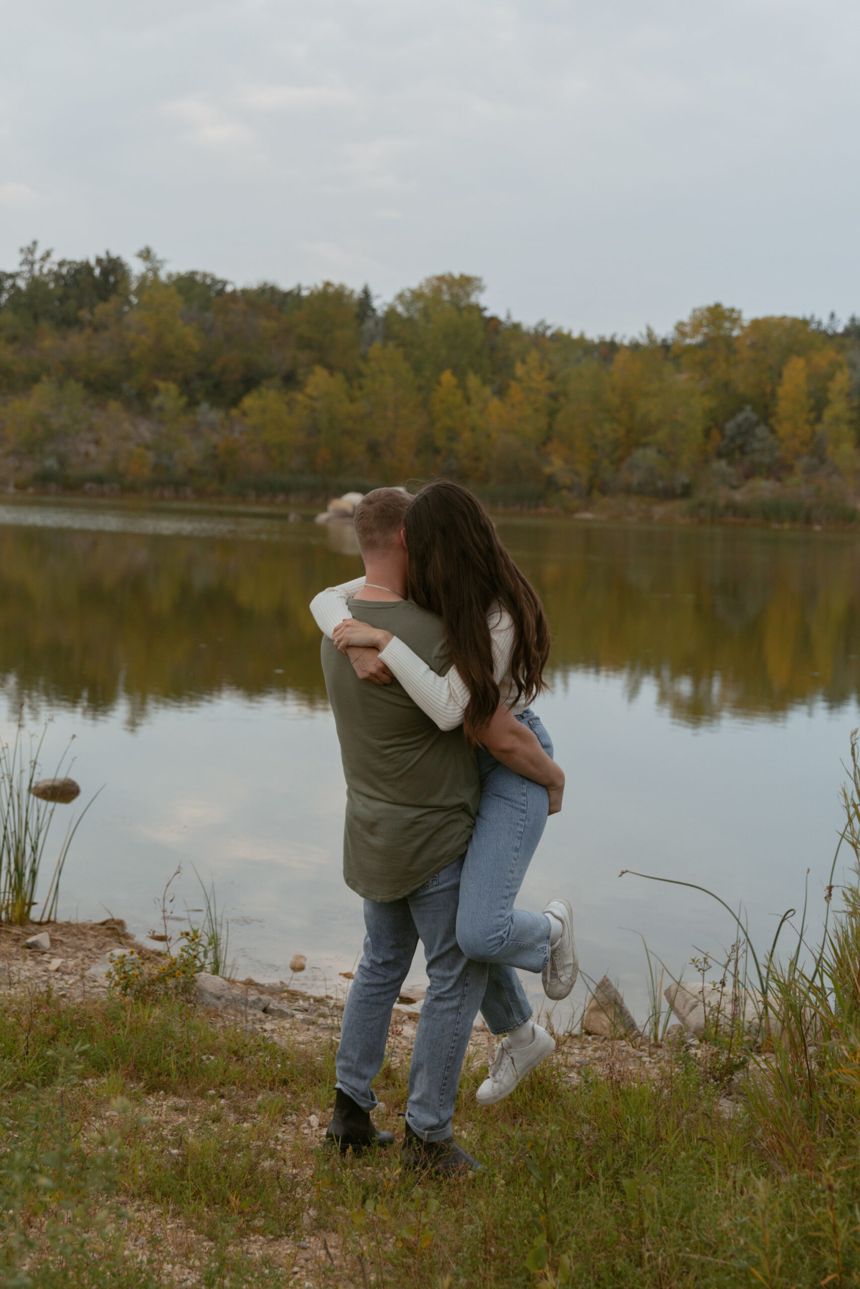 Couple hugging in front of an autumn coloured pond.