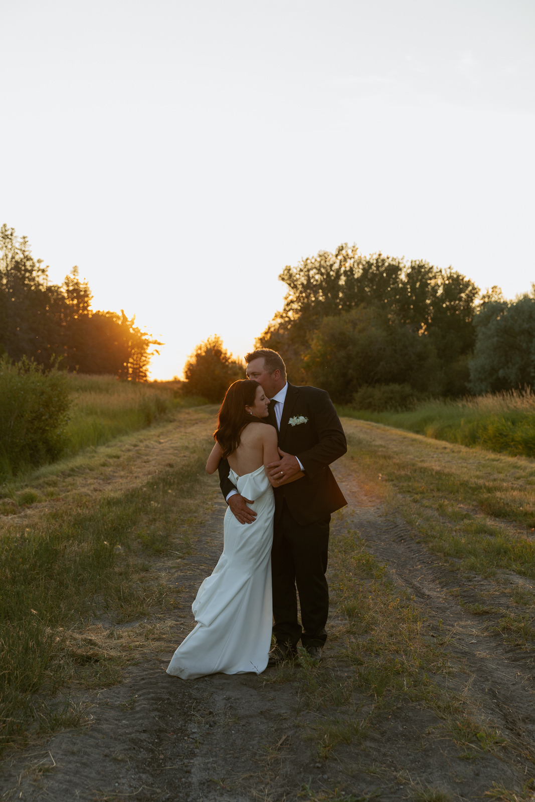 Bride and groom embracing in a field at sunset