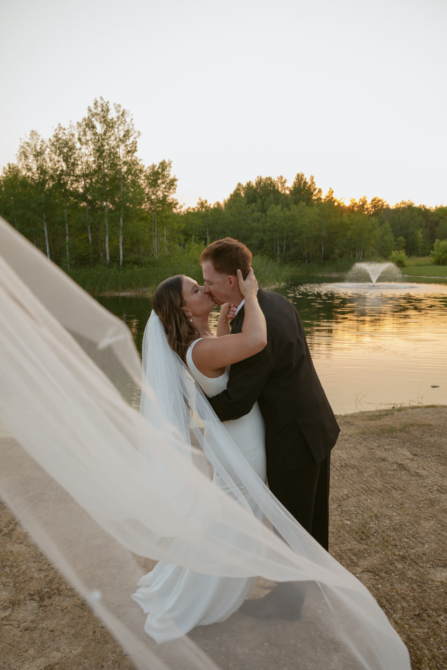 Bride and groom kissing at sunset in front of lake