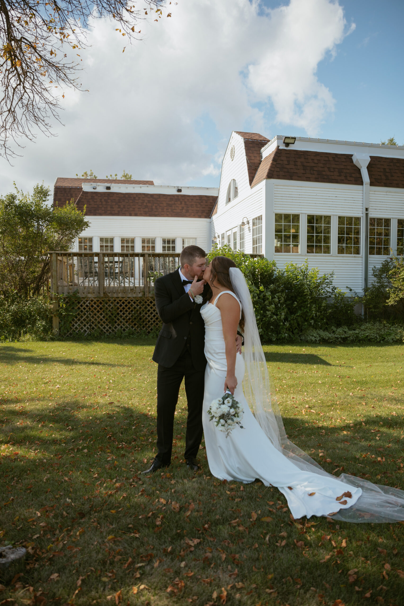 Bride & Groom kissing in front of white barn venue