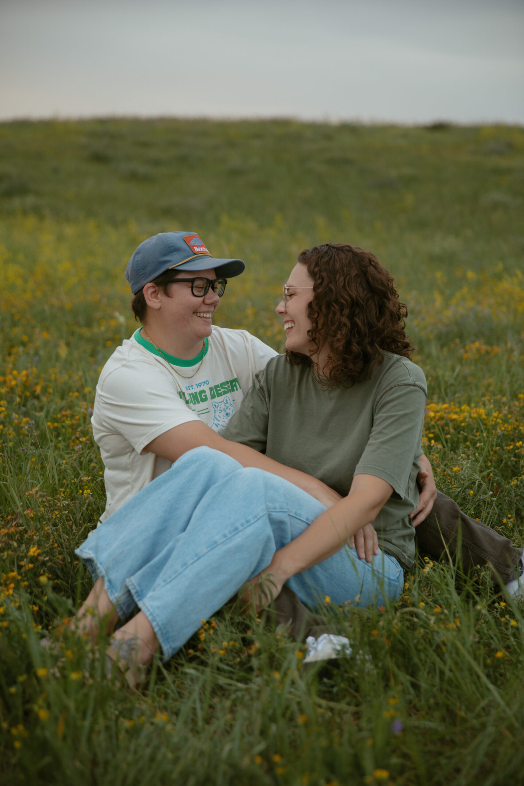 Lesbian couple sitting in a flower field together laughing