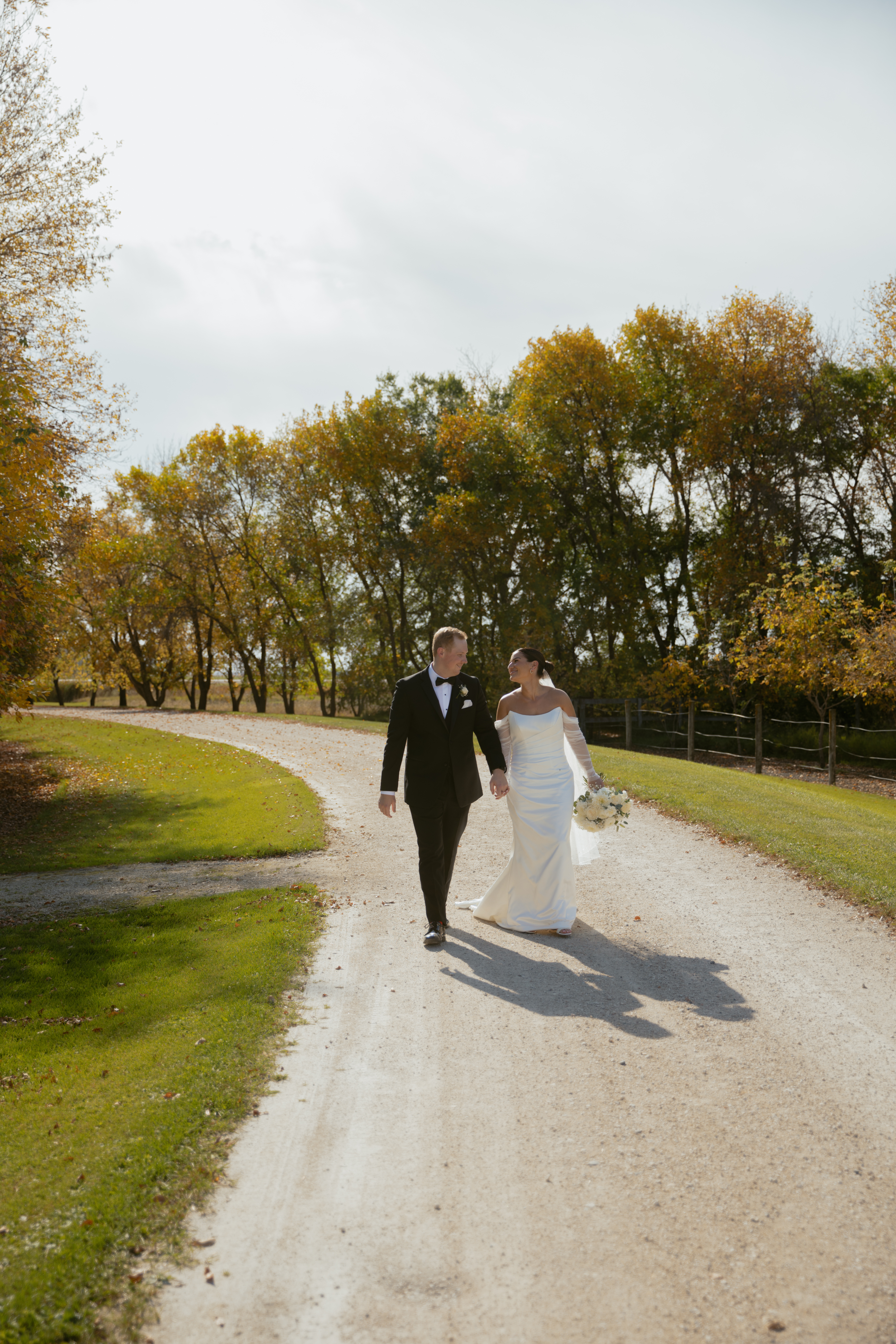 Bride & Groom walking down gravel road with autumn trees